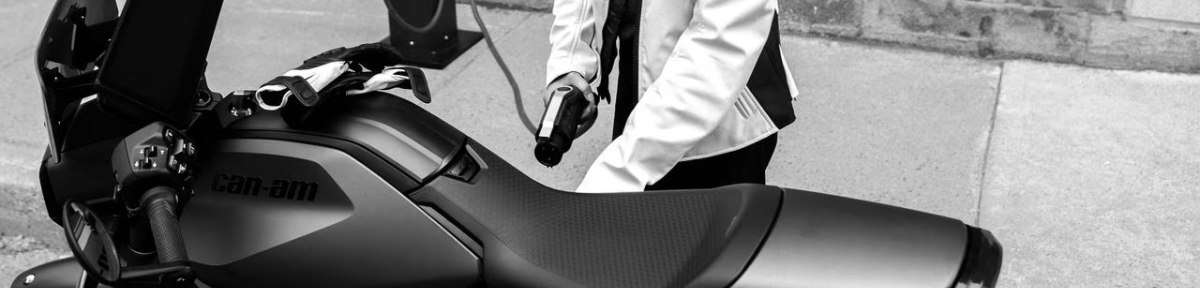 A close-up of a Can-Am EV motorcycle with a rider in Can-Am gear preparing to plug in the charger.